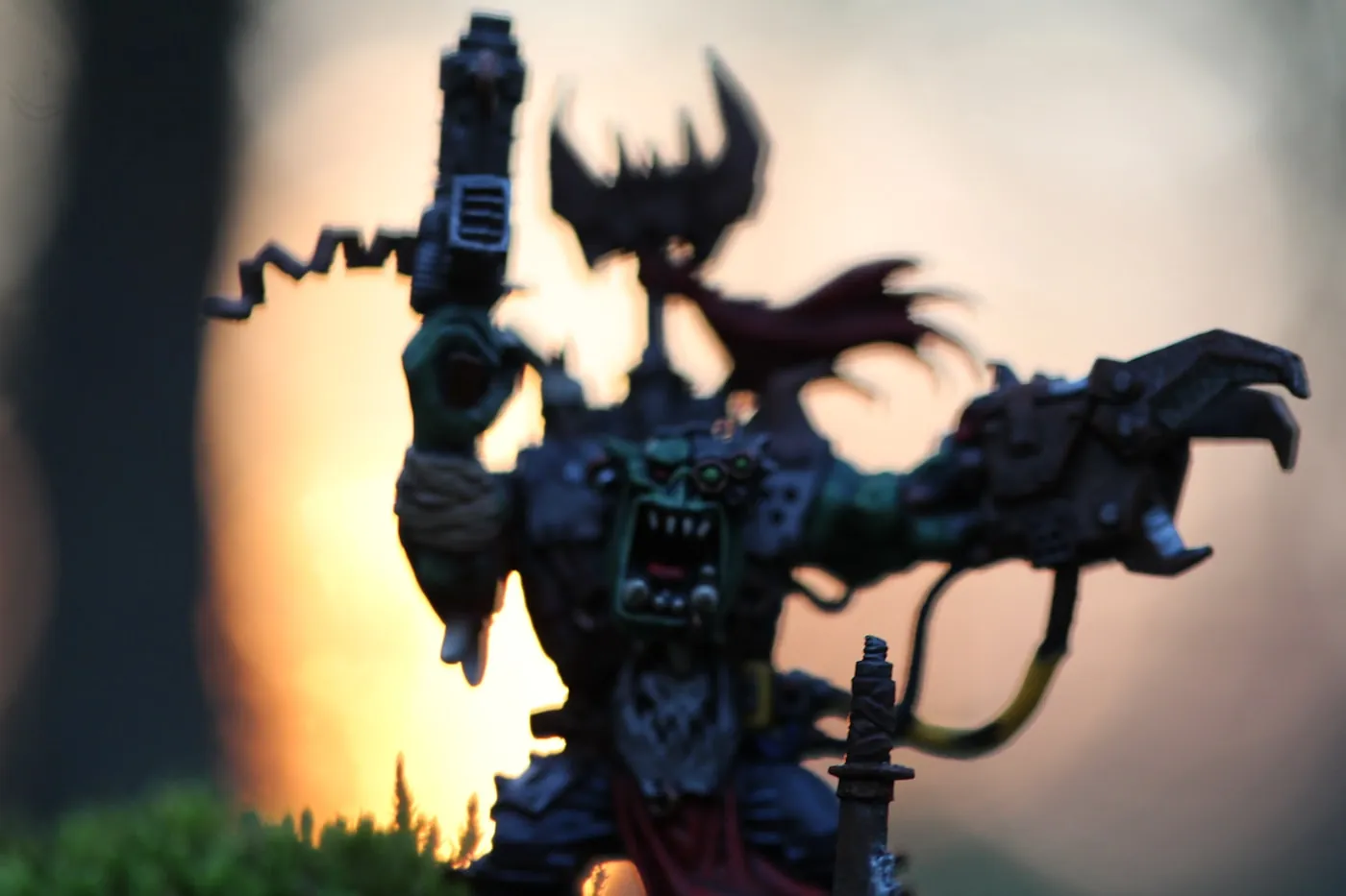 Ork warboss miniature backlit by a glowing sunset, dramatic silhouette with a red banner.